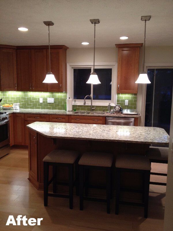 Cherry cabinetry with a green glass tile backsplash and a granite island with bar stools